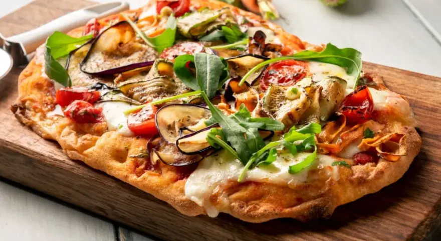 Chrupiący spód do pizzy z bakłażanem, cukinią i pomidorkami, posypany rukolą i mozzarellą.