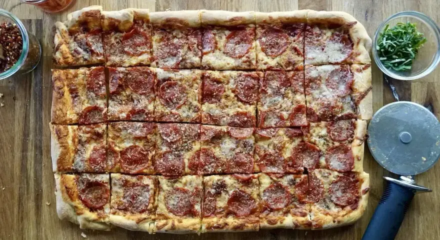 Domowa pizza na blachę z pepperoni, posypana parmezanem. Idealna na rodzinne spotkanie.