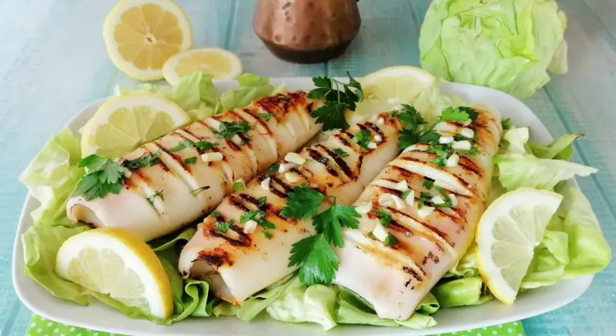 Tre calamari alla griglia, conditi con aglio e prezzemolo, serviti su un letto di lattuga con spicchi di limone.