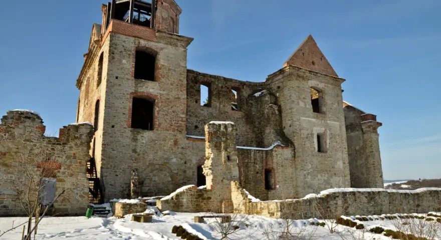 Kamienne ruiny dawnego monastyru w zimowej scenerii. Widać zniszczone mury, łuki okienne i wieżę z platformą widokową.
