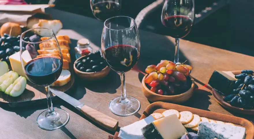 Degustacja merlot: jakie to wino? Kieliszki czerwonego wina, sery, winogrona, oliwki i pieczywo tworzą idealną kompozycję.