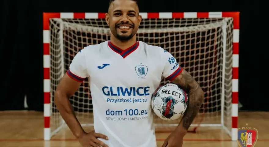 Piłkarz Piasta Gliwice w białej koszulce z piłką w ręku, na tle bramki.