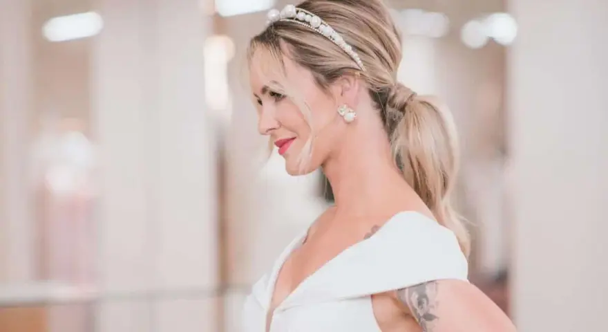 Elegancki kucyk ślubny z perłową opaską i kolczykami. Panna młoda w białej sukni z dekoltem.
