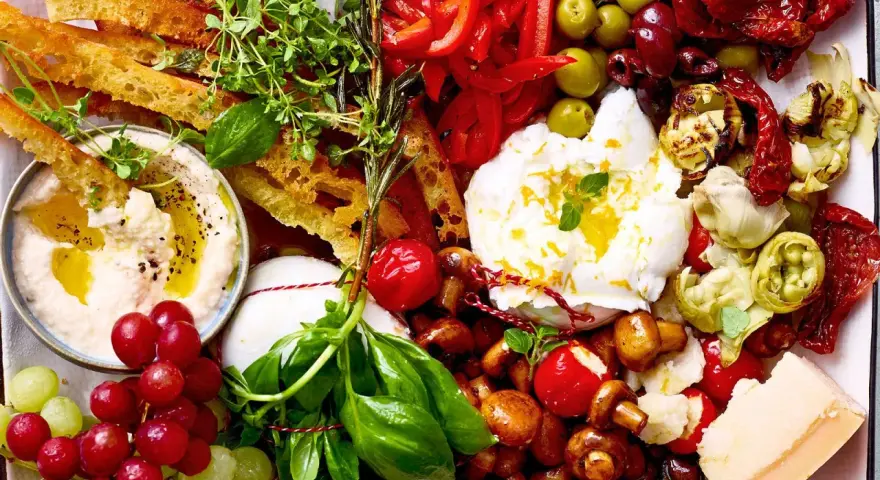 Eine Platte mit geilen Snacks: Hummus, Burrata, Trauben, Brot, Oliven, Pilze, Tomaten und Käse.