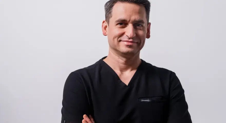 Portret mężczyzny w czarnym scrubie medycznym, ze skrzyżowanymi rękami.
