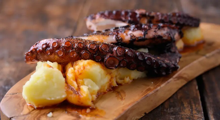 Pulpo tierno con patatas cocidas y espolvoreado con pimentón, servido en tabla de madera.