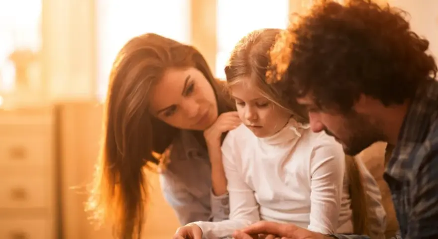 Eltern psychisch kranker Kinder spenden Trost. Ein Vater hält die Hände seiner Tochter, während die Mutter sie zärtlich berührt.