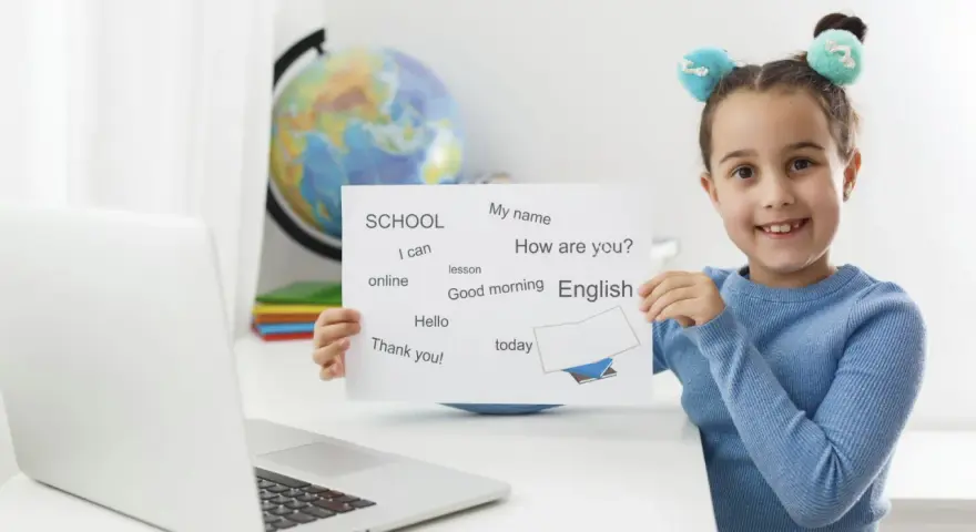 Uśmiechnięta 7 latek pokazuje kartkę z angielskimi słówkami: "English", "Hello", "Thank you!".