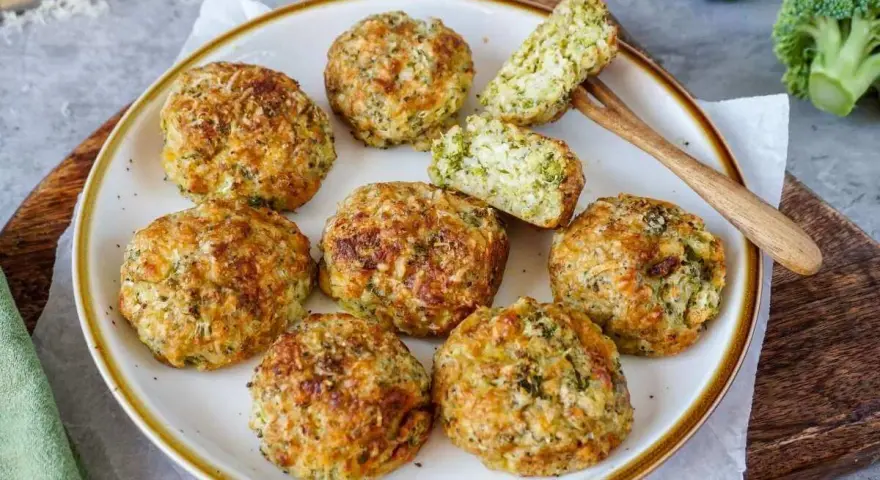 Goldbraune, knusprige broccoli nuggets auf einem Teller, ein Stück angeschnitten, mit frischem Brokkoli im Hintergrund.