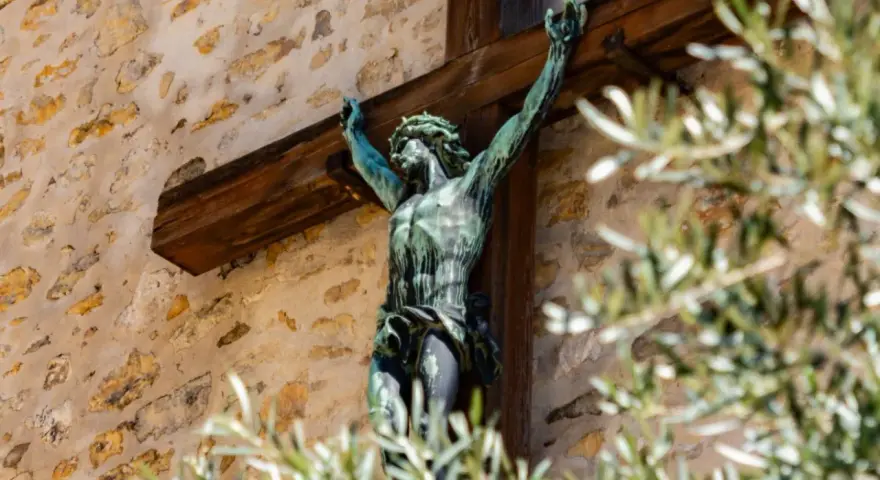 Brązowy Jezus na krzyżu, symbol chrześcijaństwa, na tle kamiennej ściany.