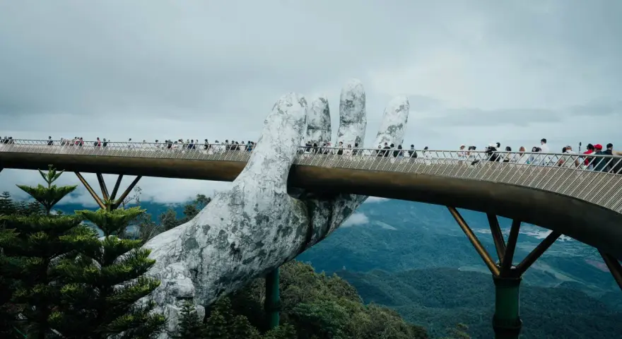 Goldene Brücke in Vietnam, gehalten von einer riesigen Steinhands. Touristen spazieren über die Brücke, die sich durch üppige grüne Berge schlängelt.