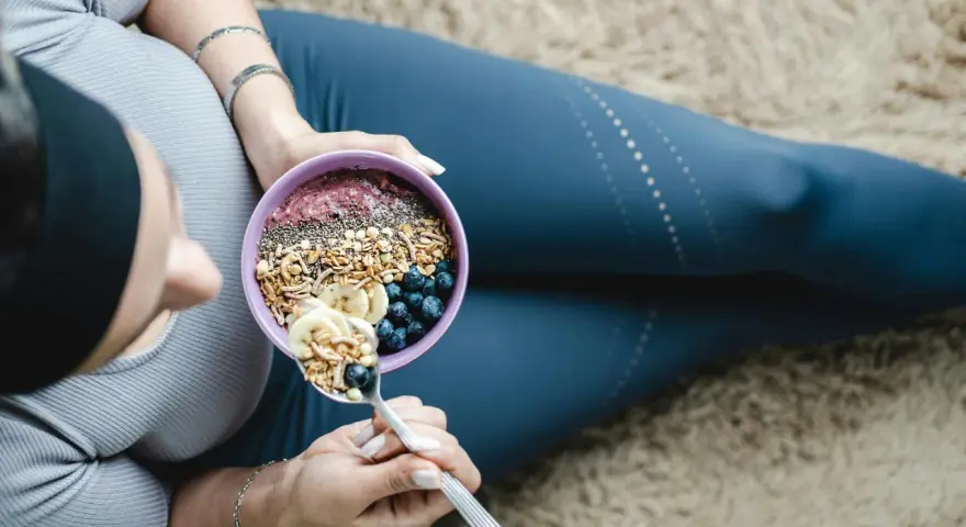 En kvinna äter en näringsrik skål med granola, bär och banan. En bra frukost kan bidra till att uppnå rekommenderat intag av hur mycket protein per dag kvinna.