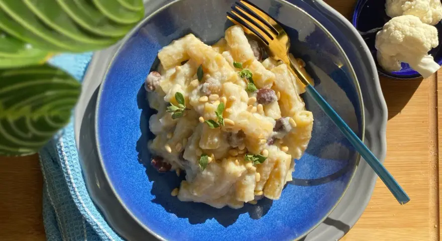 Piatto di pasta con cavolfiore cremoso, guarnito con pinoli e erbe aromatiche. Un primo piatto gustoso e leggero.