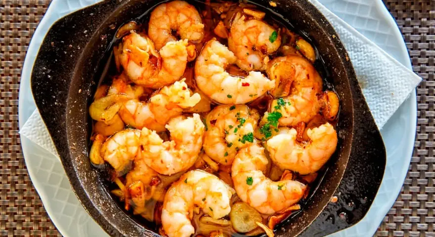 Un plato humeante de langostinos al ajillo, jugosos y dorados, nadando en aceite de oliva con ajo y perejil. ¡Un manjar irresistible!