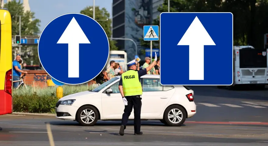 Policjant kieruje ruchem przy znakach droga jednokierunkowa. Biała Skoda czeka na sygnał.