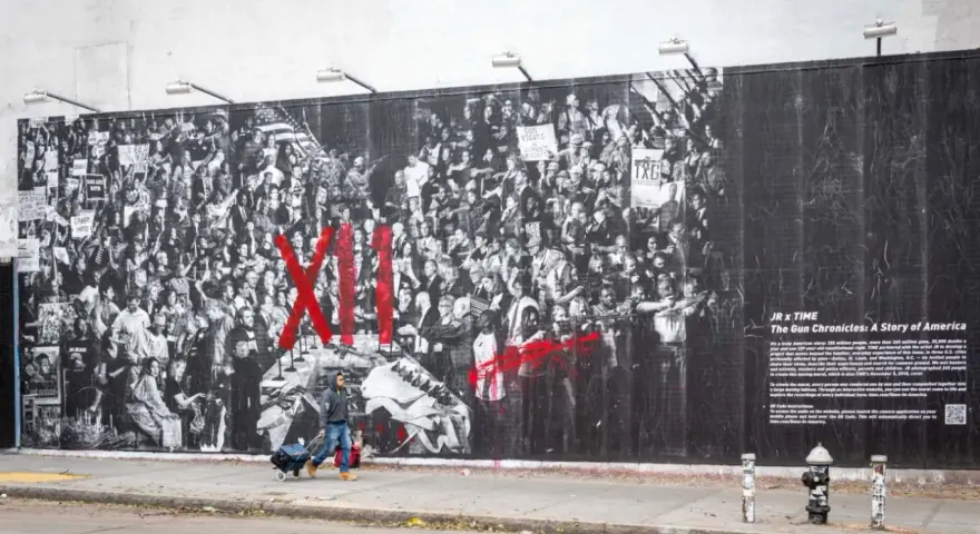 Une fresque murale de street art d'origine, "The Gun Chronicles: A Story of America", par JR x TIME, dépeint une foule en noir et blanc avec des touches de rouge vif.