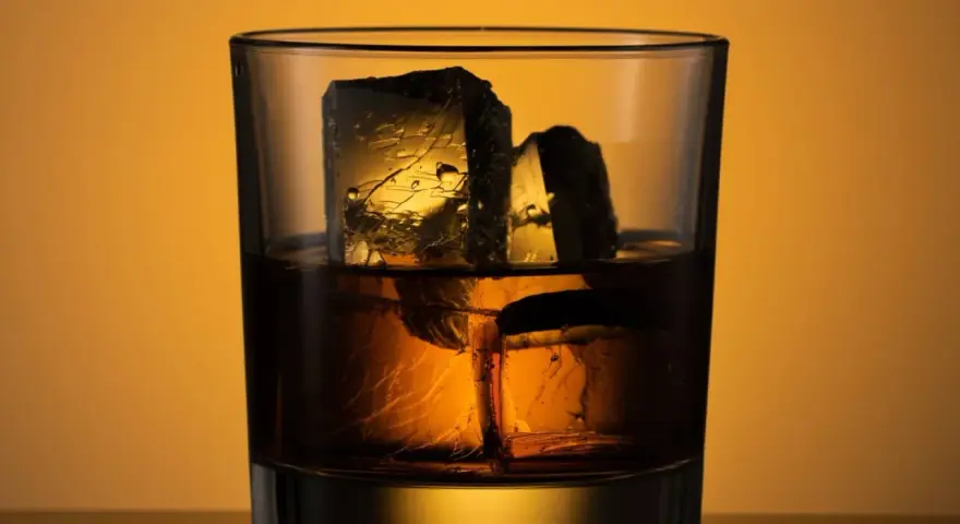 Ein Glas mit **whiskey neat**, zwei große Eiswürfel darin, beleuchtet von warmem Licht.