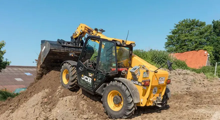 Żółty ładowarka teleskopowa JCB 525-60 z podniesionym wysięgnikiem i łyżką, pracująca na budowie.