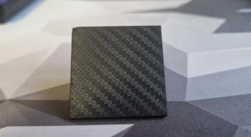A small cube with a textured surface, showcasing the intricate pattern achieved through carbon fiber 3D printing.