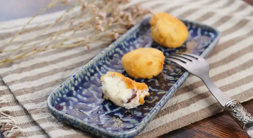 Croquetas de jamón doradas y cremosas en plato azul, una partida.