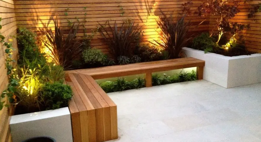 Elegante decoracion patio interior con banco de madera y plantas iluminadas.