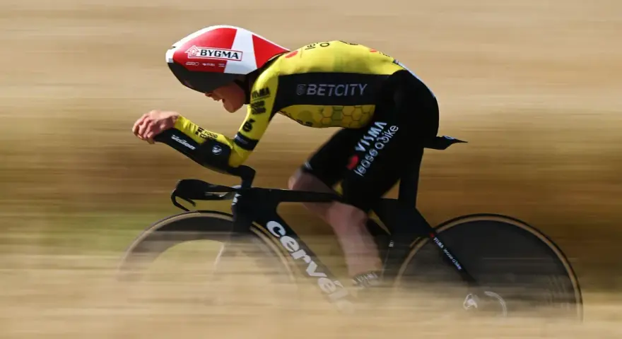 A cyclist in a yellow and black suit, helmet, and aero bars races during the Dauphine cycling event, blurring past the camera.