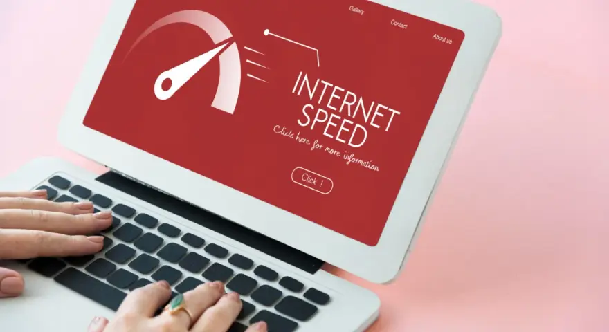 Schermo di un laptop con indicatore di velocità internet su sfondo rosso. Le mani digitano sulla tastiera, frustrati dall'internet lento.
