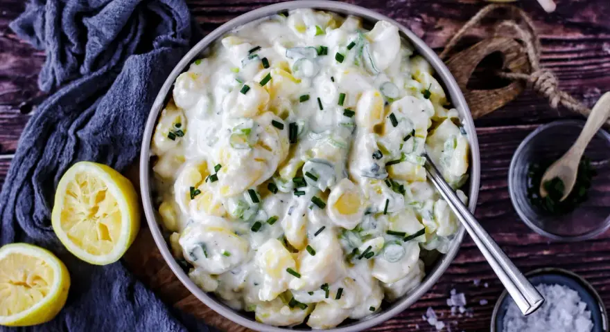 Cremiger Kartoffelsalat mit Joghurt, garniert mit Schnittlauch. Dazu passen frische Zitronenspalten.
