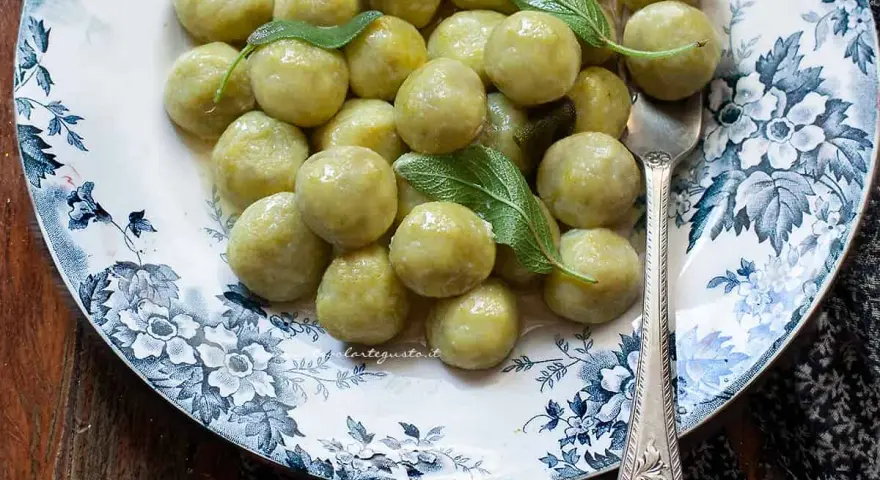 Gnocchi di zucchine morbidi e profumati, guarniti con foglie di salvia fresca su un piatto decorato.