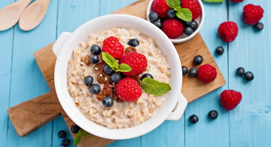 Un tazón de avena con frambuesas, arándanos y pasas. Descubre los beneficios de la avena por la noche para un descanso reparador.