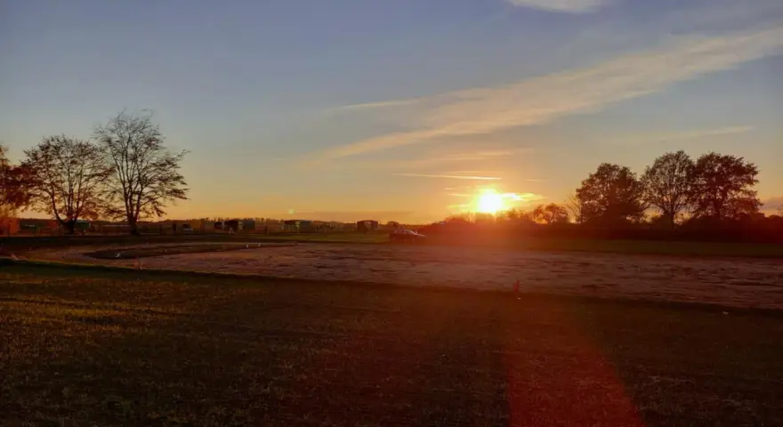 Sonnenuntergang über einem Feld mit Bäumen und einem Auto. "Seid stille und wisset: Ich bin Gott." (Psalm 46:10)