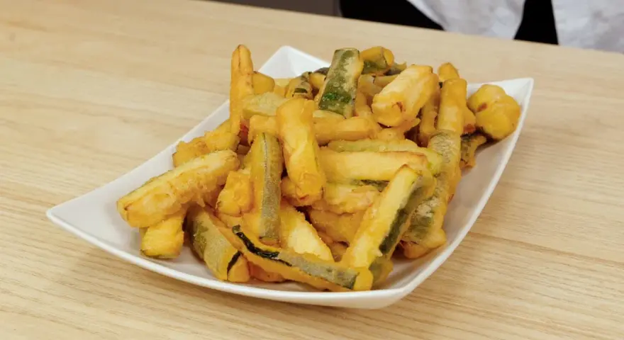 Un piatto bianco pieno di zucchine in pastella dorate e croccanti, pronte per essere gustate.