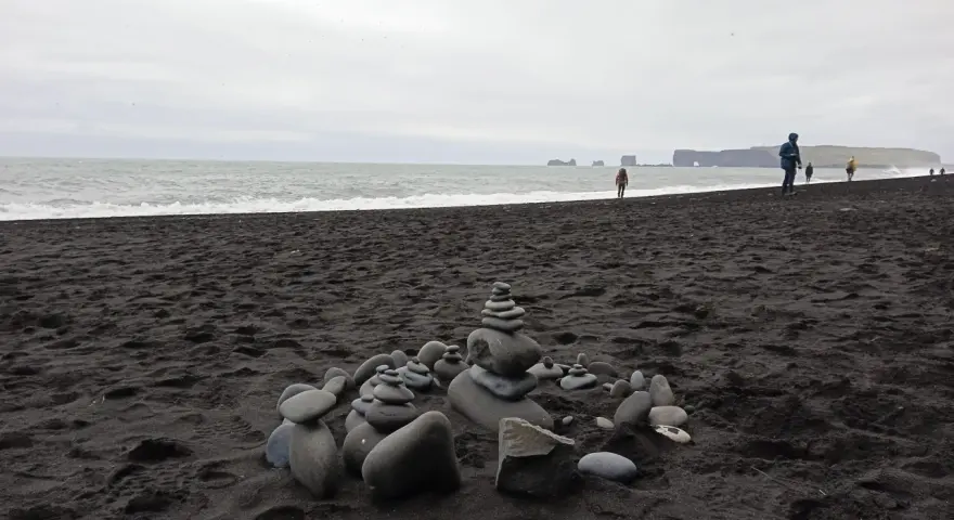 Kamienne stosy na czarnej plaży Islandii, z widokiem na ocean i skaliste wybrzeże.