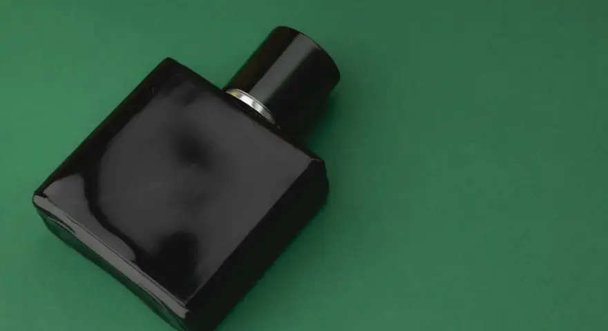 Czarna, elegancka butelka perfum z nutą wetiwery na zielonym tle.