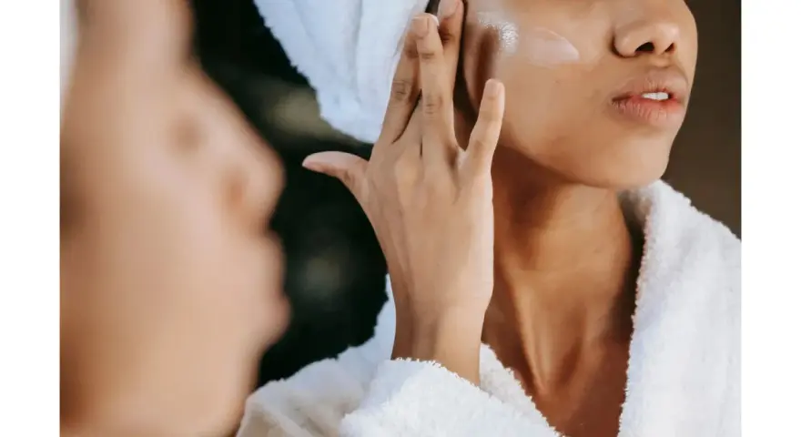 Une femme applique une crème hydratante sur sa joue, un geste essentiel pour savoir comment bien hydrater son visage et obtenir une peau éclatante.