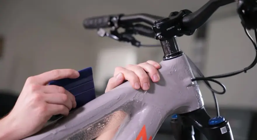 Hands apply protective film to a mountain bike frame. This bike is ready for any terrain, whether trails or roads.