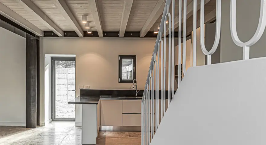 Interno moderno con travi a vista in legno, illuminazione led soffusa e una scala bianca.