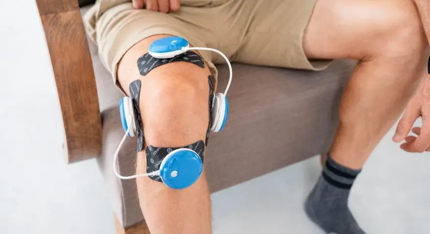 Un homme utilise un appareil d'électrostimulation pour son genou, une solution pour le traitement de la tendinite du genou.