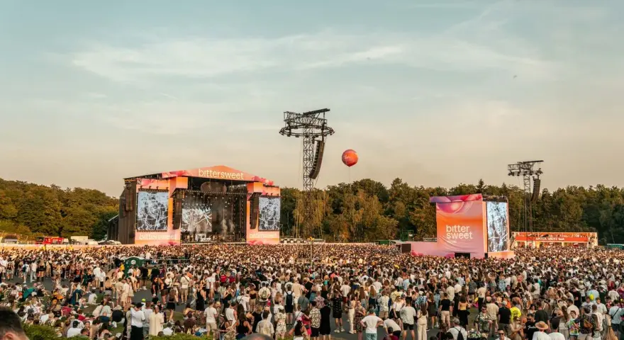 Tłum ludzi na festiwalu bittersweet, dwie sceny, ekrany z grafikami i pomarańczowy balon na niebie.