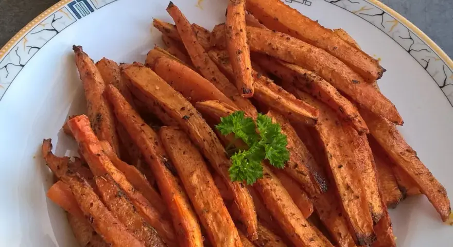 Stos pieczonych frytek z marchewki z natką pietruszki na talerzu.