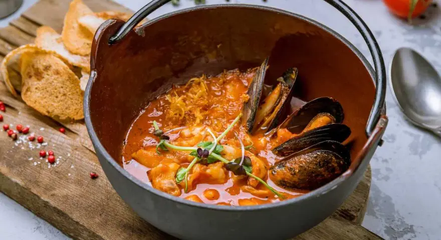 Un delicioso suquet de peix, con mejillones y gambas en una cazuela de barro, acompañado de tostadas.