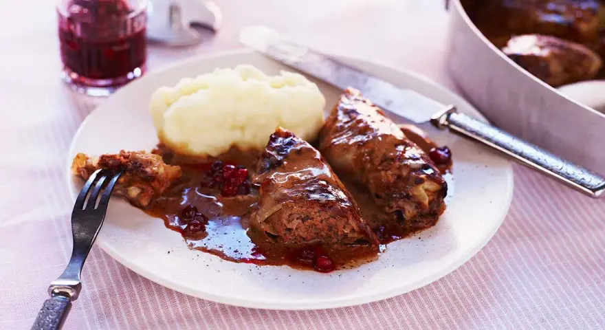 Kåldolmar recept: två saftiga kåldolmar med potatismos och lingonsylt, serverade med en mustig sås.
