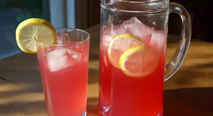 En karaff och ett glas med rosa lemonad, is och citronskivor. Perfekt för ett enkelt lemonad recept.