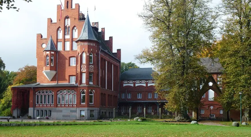Das imposante Schloss Kalkhorst, ein Backsteinbau mit Türmchen und Erkern, steht im Herbstlicht.