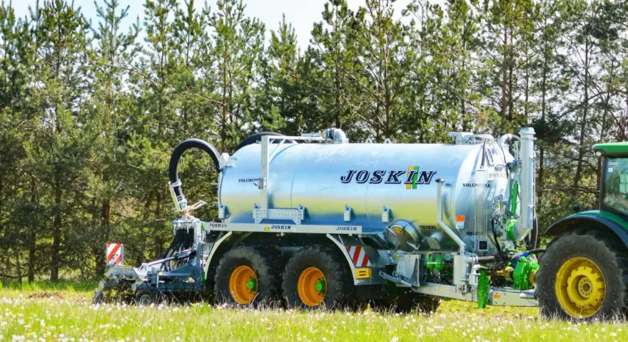 Cysterna JOSKIN na polu, gotowa do rozrzucenia gnojowicy lub gnojówki. Zielony traktor czeka w tle.