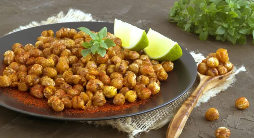 Ceci croccanti al forno, conditi con paprika e guarniti con basilico fresco e spicchi di lime, invitano a uno snack salutare e gustoso.