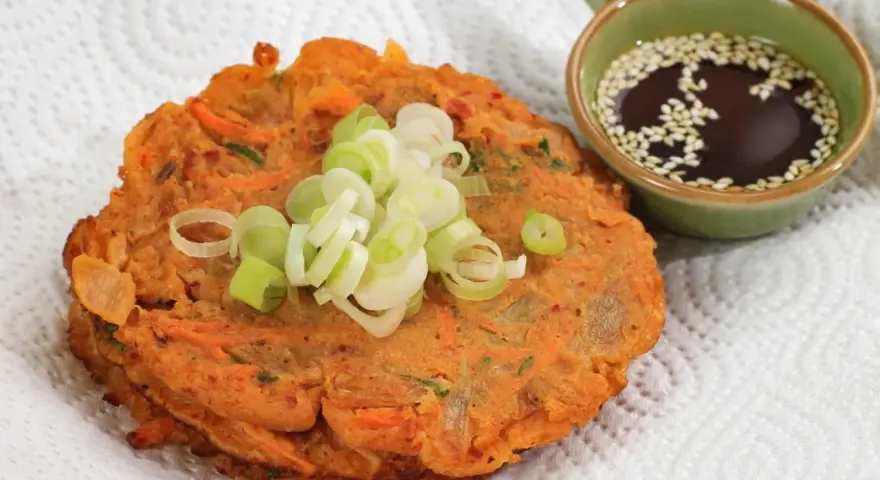 Chrupiące placki z kimchi, posypane szczypiorkiem, obok miseczki z sosem sezamowym. Idealne na przekąskę.