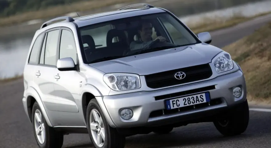 Srebrny SUV Toyota RAV4 na drodze, z kierowcą za kierownicą.