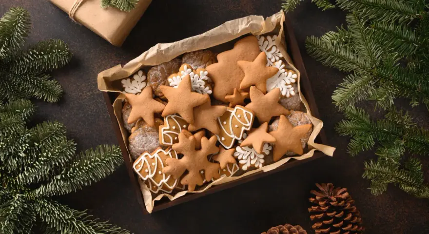 Last minute weihnachtsgeschenke selber machen: Eine Schachtel voller liebevoll verzierter Lebkuchen in Stern- und Baumform, umgeben von Tannenzweigen und Kiefernzapfen.