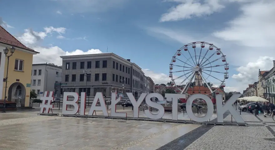 #Białystok - wielki napis zaprasza do odkrywania atrakcji miasta, w tle koło widokowe i zabytkowa zabudowa.